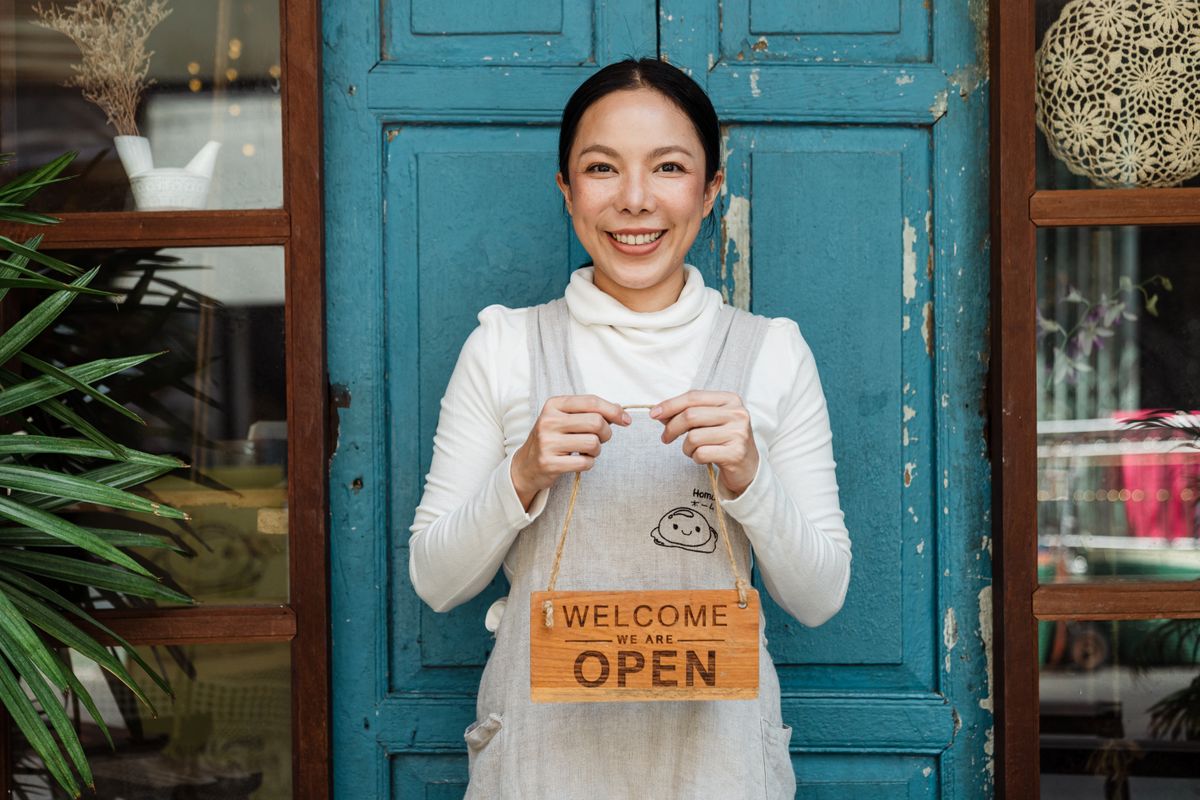 Une commerçante souriante accueille ses clients, pancarte ouverte à la main