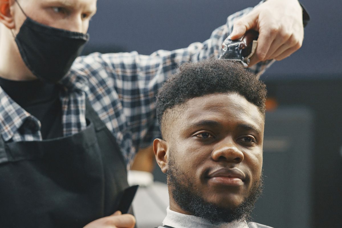 Un coiffeur coupe les cheveux d'un client souriant dans son salon